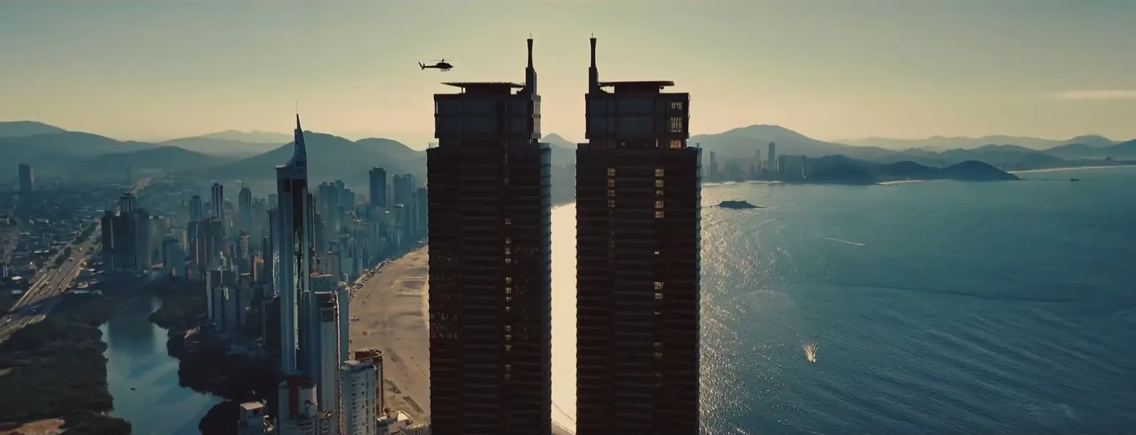 Duas torres residenciais ao pôr do sol, com a cidade e o mar ao fundo